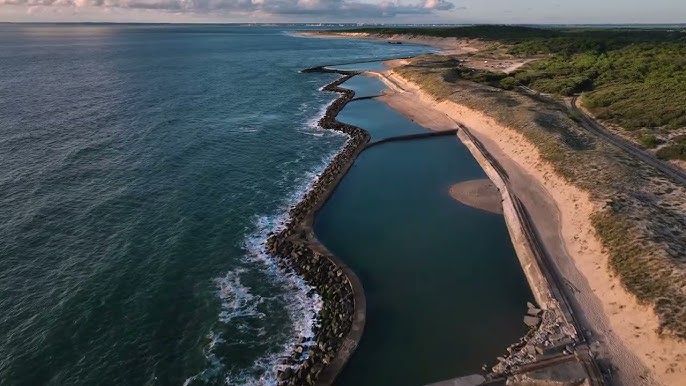Piscines de mer et digue rocheuse sur le littoral Bassins d'eau de mer protégés par une digue sur une plage sauvage bordée d'une forêt de pins.